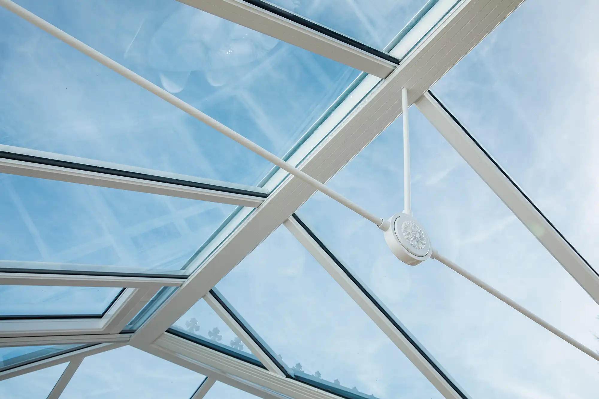 Glass ceiling panels with white frame and cross supports, allowing natural light and a view of a blue sky.